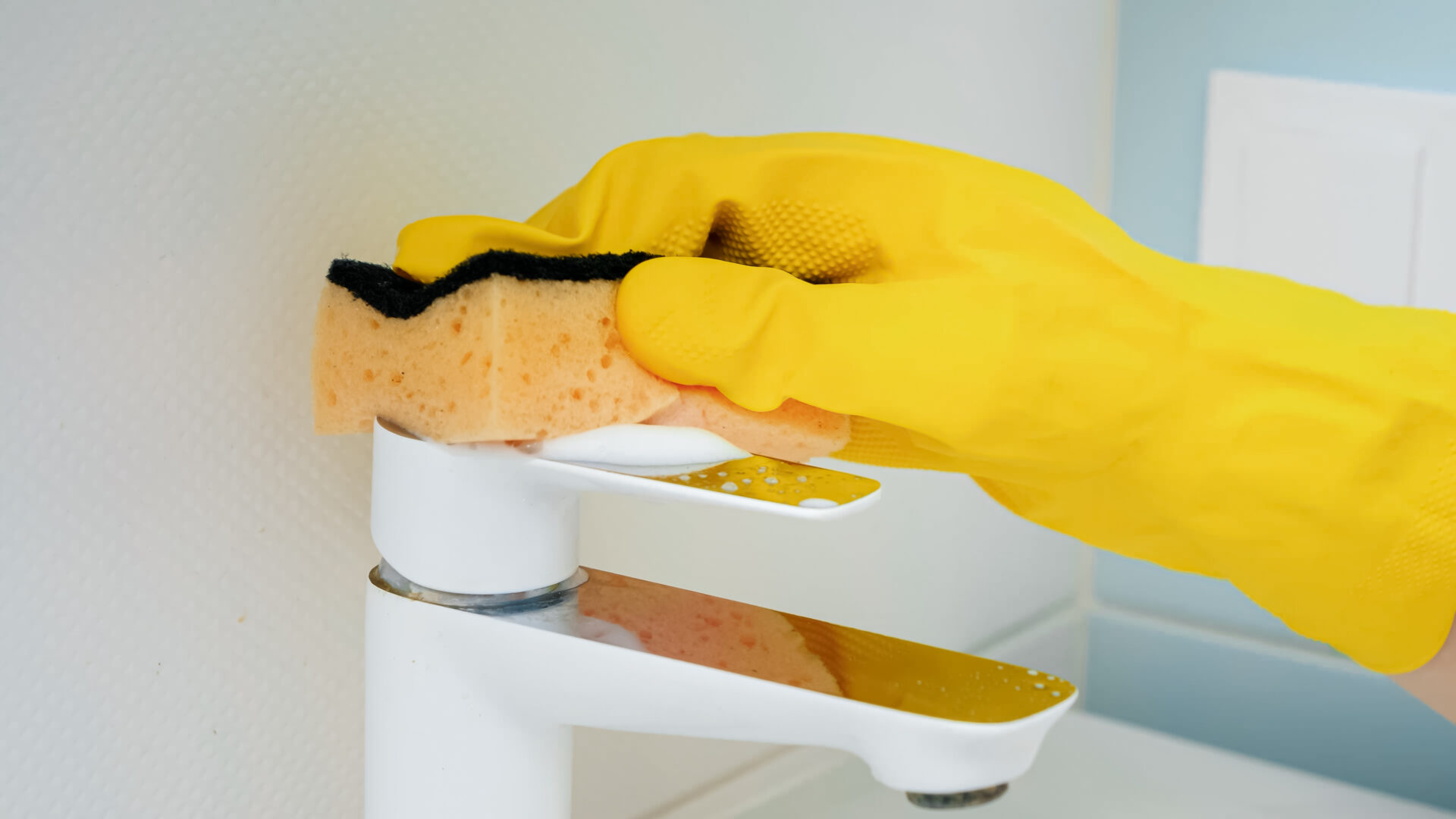 Coseup of hand wearing yellow rubber glove washing and cleaning water faucet in bathroom